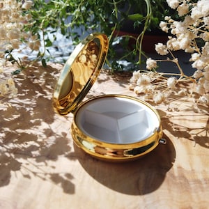 K&ouml;nnte beinhalten: Eine goldene Pillendose mit einem wei&szlig;en Innenraum, der in drei Abschnitte unterteilt ist. Die Dose ist ge&ouml;ffnet und der Deckel liegt auf der Seite.