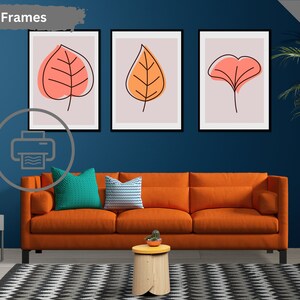 May include: Three printable wall art prints featuring abstract leaf designs in shades of orange and pink on a light pink background. The prints are displayed in a living room setting with a couch, side table, and plant.