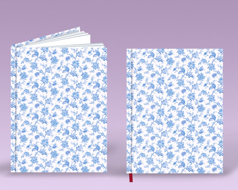 May include: Two white notebooks with a blue floral pattern. The notebook on the left is open, showing blank pages. The notebook on the right is closed and has a red ribbon bookmark.