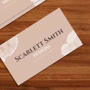 Pode incluir: Um cart&atilde;o de visita de cor castanho claro com o texto "SCARLETT SMITH DESIGNS" em letras castanho escuras. O cart&atilde;o tem um design de aquarela com formas abstratas brancas e castanhas claras.