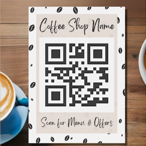 May include: A white sign with a black and white QR code and the text "Coffee Shop Name" and "Scan for Menu & Offers".