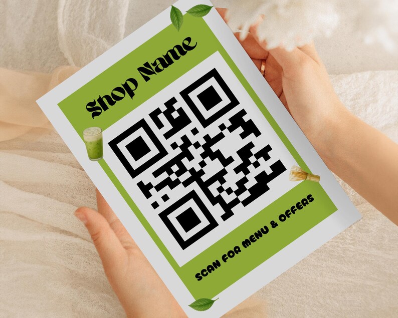 May include: A white and green printed card with the text "Shop Name" and a large QR code. The card also includes the text "SCAN FOR MENU & OFFERS". The card is held by a person.
