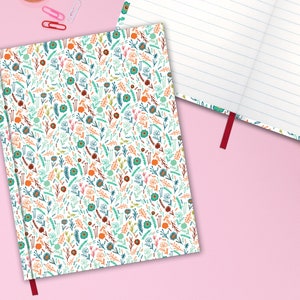 May include: A white notebook with a red ribbon bookmark. The cover features a repeating pattern of colorful flowers and leaves.