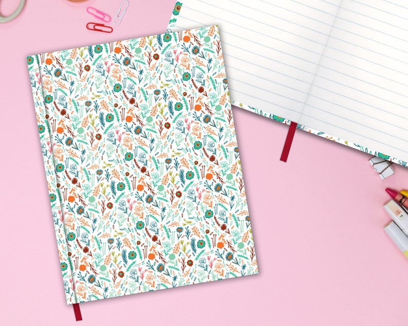 May include: A white notebook with a red ribbon bookmark. The cover features a repeating pattern of colorful flowers and leaves.