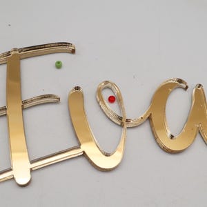 Può includere: Cartello con nome in acrilico a specchio dorato con il nome "Eva" in scrittura corsiva.