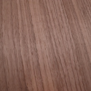 May include: Close-up of a wood grain surface with a reddish-brown color. The grain is straight and runs diagonally across the image.