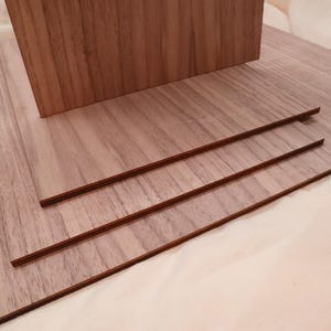 May include: Four pieces of wood veneer stacked on top of each other. The wood has a light brown color and a wood grain pattern.