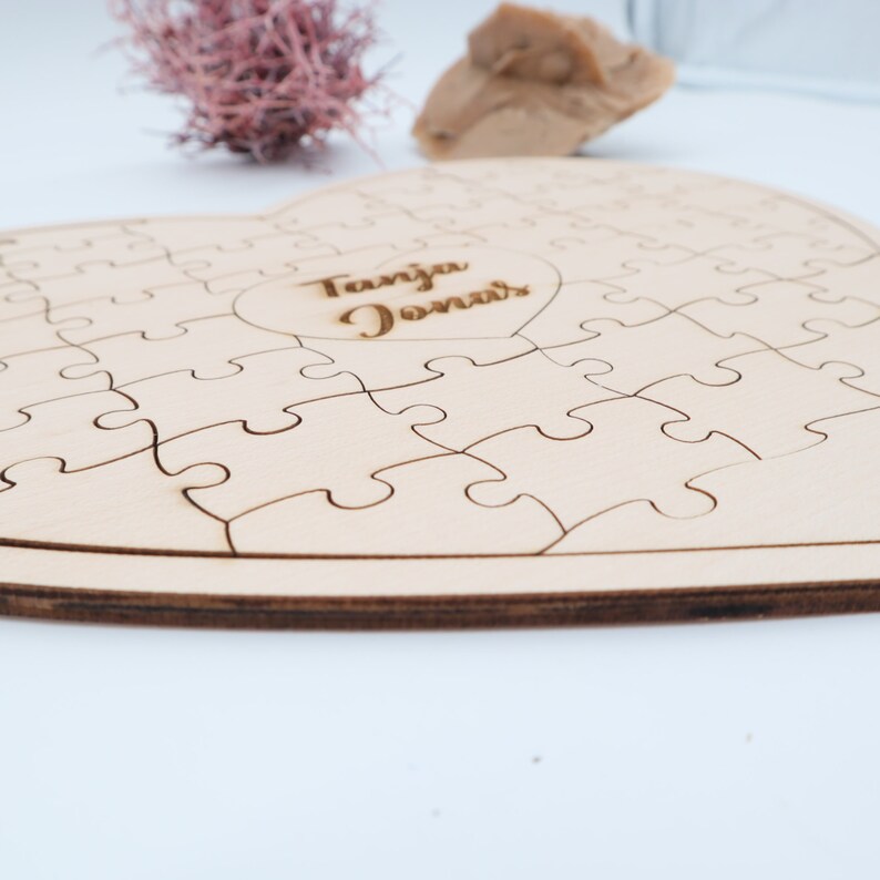 May include: A wooden heart-shaped jigsaw puzzle with a smaller heart cutout in the centre. The cutout heart has the names "Tanja Jonas" engraved inside.