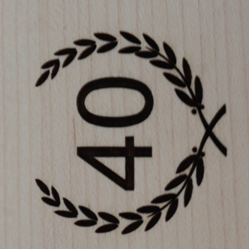 May include: A black and white image of the number 40 surrounded by a wreath of leaves. The number 40 is centred in the image and the wreath of leaves is around the outside of the number.