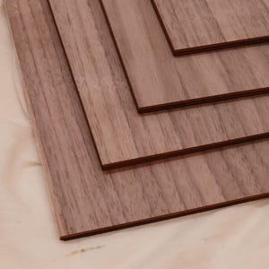 May include: Four pieces of wood veneer, each with a different wood grain pattern, are stacked on top of each other. The wood is a light brown color with a reddish hue.