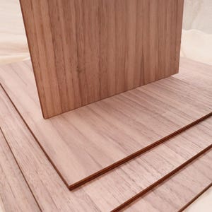 May include: Stack of four light brown wood panels with a wood grain pattern. The panels are stacked on top of each other, with the top panel slightly offset from the others.