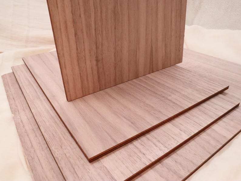 May include: Stack of four light brown wood panels with a wood grain pattern. The panels are stacked on top of each other, with the top panel slightly offset from the others.