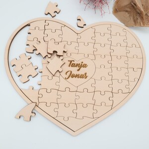 May include: A wooden heart-shaped jigsaw puzzle with the names "Tanja Jonas" engraved in the centre. The puzzle is partially assembled, with some pieces missing.