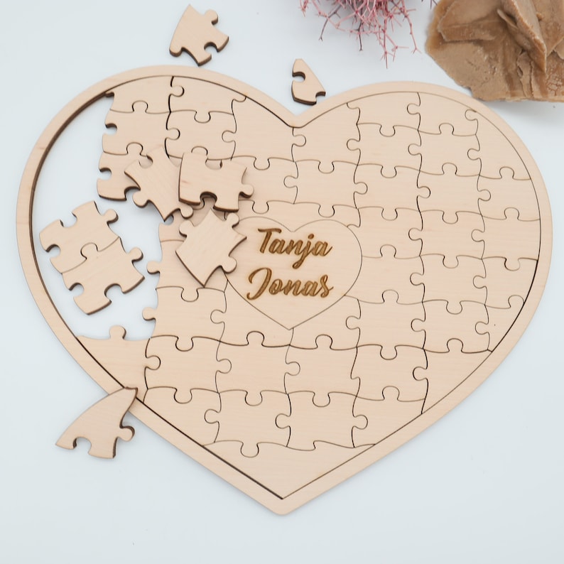 May include: A wooden heart-shaped jigsaw puzzle with the names "Tanja Jonas" engraved in the centre. The puzzle is partially assembled, with some pieces missing.