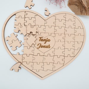 May include: A wooden heart-shaped jigsaw puzzle with the names "Tanja Jonas" engraved in the centre. The puzzle is partially assembled, with some pieces missing.