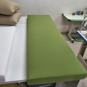 May include: A rectangular, lime green cushion with a stitched edge. The cushion is placed on a white surface, with two beige pillows in the background. A sewing table is visible in the background.