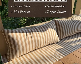May include: Custom outdoor cushions with a striped pattern in beige and white. The cushions are on a wooden surface. The image includes text that says "Custom Outdoor Cushions", "Custom Size", "50+ Fabrics", "Stain Resistant", and "Zipper Covers".
