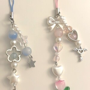 May include: Two phone charms with a variety of beads and charms. One charm features a blue and white color scheme with stars, flowers, and a heart-shaped lock. The other charm features a pink and white color scheme with a bow, hearts, a key, and a tulip.