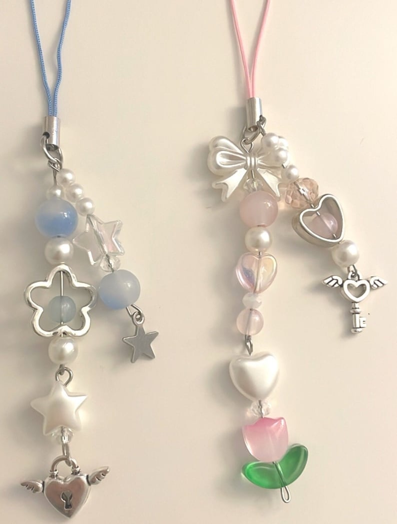 May include: Two phone charms with a variety of beads and charms. One charm features a blue and white color scheme with stars, flowers, and a heart-shaped lock. The other charm features a pink and white color scheme with a bow, hearts, a key, and a tulip.