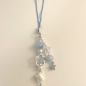 May include: A blue and white charm with a heart lock, stars, and beads. The charm is attached to a blue string.