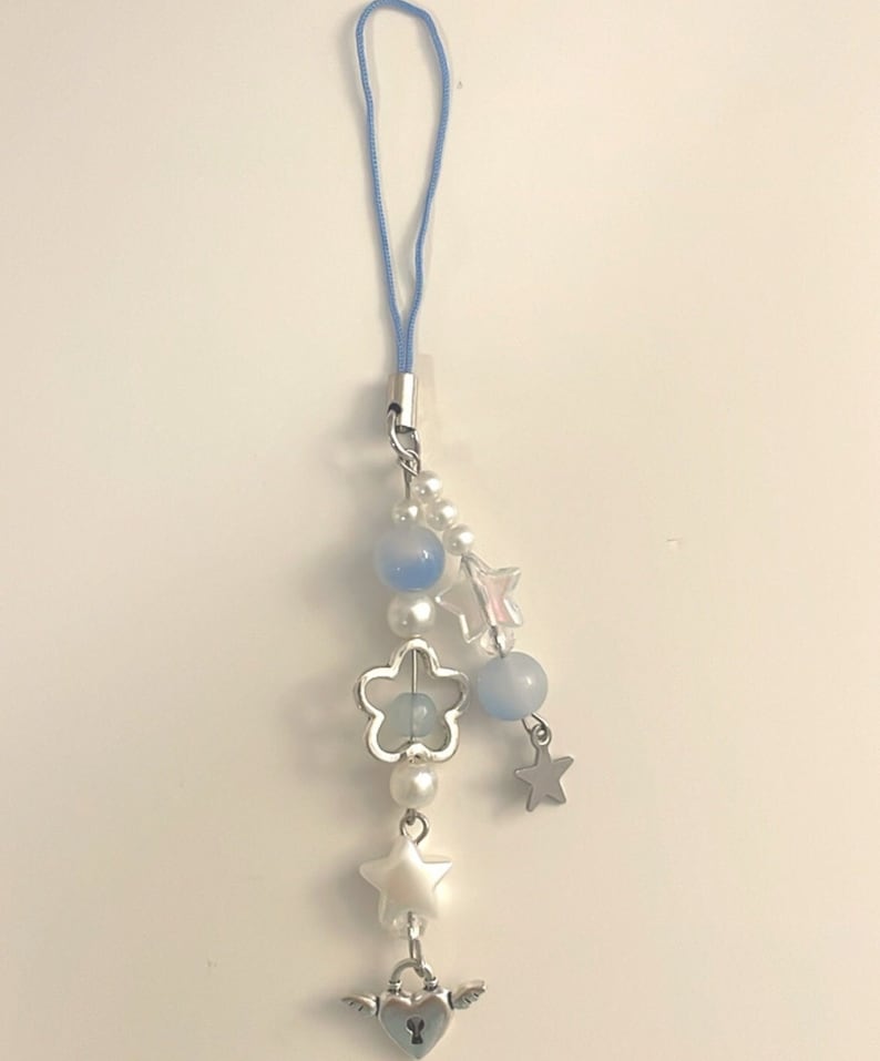 May include: A blue and white charm with a heart lock, stars, and beads. The charm is attached to a blue string.