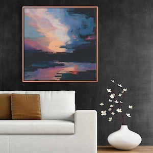 May include: Abstract landscape painting in a copper-colored frame. The artwork features a blend of blues, pinks, and oranges, creating a sunset or sunrise effect. The painting hangs above a white sofa with brown throw pillows.