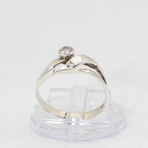 May include: A silver ring with a single clear stone set in a swirl design.