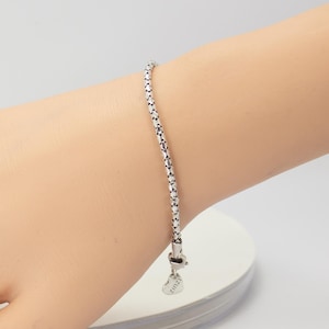 May include: A silver bracelet with a textured chain design is shown on a wrist. The bracelet has a heart-shaped charm with the word "zinzi" engraved on it. The bracelet is a delicate piece of jewellery.
