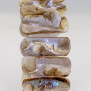 Op de afbeelding: Een armband gemaakt van iriserende witte en bruine schelpstukken. De stukken zijn verbonden door een doorzichtig touwtje.