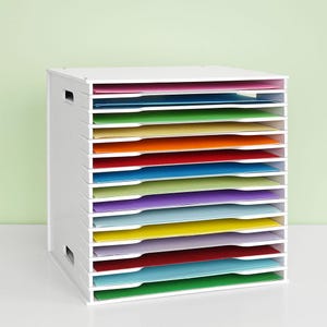 May include: White paper storage organizer with 12 slots for storing different colored paper. The organizer is made of white plastic and has a handle on the side.