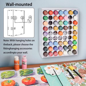 May include: White wall-mounted paint storage rack with 36 slots for paint bottles. The rack is shown with colorful paint bottles in each slot. The rack is mounted on a wall with a white background. The image also shows a table with a painting surface, paint brushes, and a paint palette.