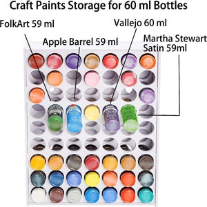 May include: White paint storage rack with 60 holes for 60 ml bottles. The rack is filled with various colors of paint bottles, including FolkArt, Vallejo, Apple Barrel, and Martha Stewart Satin.
