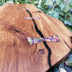 May include: A wooden serving tray with a black epoxy river and colorful pencil bowties. The tray is made of natural wood with a rustic finish.