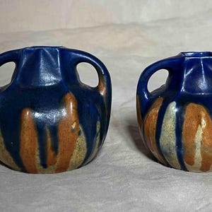 Può includere: Due piccoli vasi in ceramica blu e marrone con due manici ciascuno. I vasi hanno una smaltatura screziata con striature marroni e bianche.