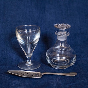 Peut inclure: Un flacon en verre transparent avec un bouchon, un verre à pied en verre transparent et une cuillère à cocktail en argent sur un fond bleu.