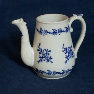 Op de afbeelding: Een witte theepot van keramiek met een blauw en wit bloemenpatroon. De theepot heeft een tuit en een handvat.