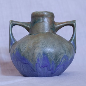 Puede incluir: Un jarrón de cerámica azul y verde glaseado con dos asas. El jarrón tiene un efecto moteado, marmoleado.
