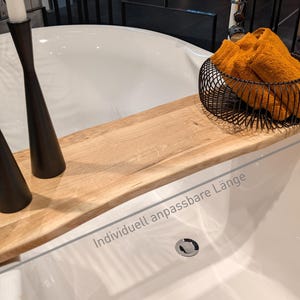 May include: A wooden bathtub tray with a natural finish, holding two black candle holders with white candles and a black wire basket filled with orange towels. The text "Individuell anpassbare L&auml;nge" is visible.