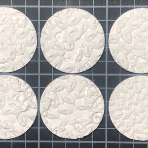 May include: Six white ceramic round tiles with a repeating pattern of embossed faces. The tiles are arranged in two rows of three.