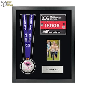 May include: Black framed display featuring a London Marathon finisher's medal with a purple ribbon, a race bib, and a photo of runners. Includes space for custom text. The frame is from Deluxe DIY Displays.