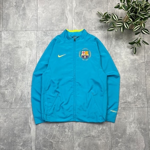 Può includere: Una giacca blu chiaro con chiusura a zip e un logo Nike Swoosh giallo sul petto sinistro. La giacca ha un piccolo stemma ricamato del FC Barcelona sul petto destro. La giacca ha una zip gialla e un cappuccio con coulisse giallo.
