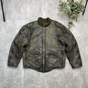 Puede incluir: Chaqueta de cuero verde oliva vintage con cuello de canalé y cierre de cremallera. La chaqueta presenta un diseño acolchado y dos bolsillos delanteros. El texto "DEEP LIMIT LEATHER" es visible en la parte inferior derecha.