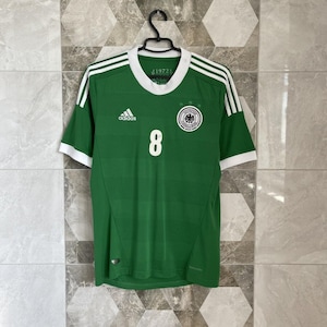 May include: Green soccer jersey with white accents, featuring the number 8 and the German national team emblem. The Adidas logo is visible on the chest. The jersey has white stripes on the shoulders and a white collar.
