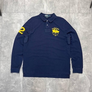 Puede incluir: Polo de manga larga azul marino con un número 2 amarillo en la manga izquierda. La camisa presenta un logotipo amarillo con el texto "POLO RALPH LAUREN New York, NY 1967".