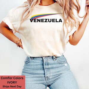 May include: A white t-shirt with a graphic of the Venezuelan flag and the word "VENEZUELA" in black text.