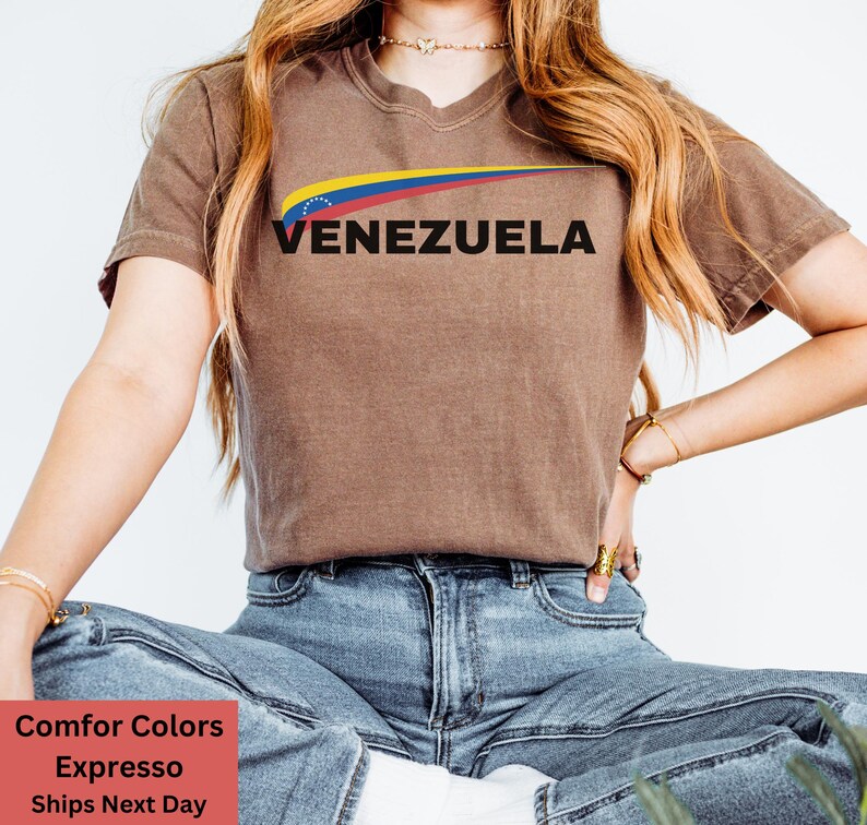May include: A brown t-shirt with a yellow, blue, and red graphic of the Venezuelan flag and the word "VENEZUELA" in black text.