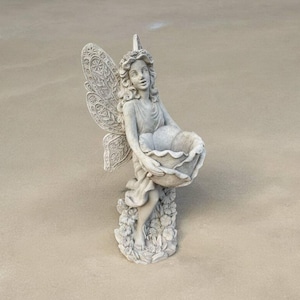 May include: A detailed, light gray fairy statue with intricate wing and floral details. The fairy is holding a large, shell-shaped bowl. The statue is standing on a base with floral accents, creating a whimsical garden decor piece.