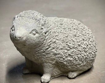 May include: A gray concrete sculpture of a hedgehog. The hedgehog is curled up in a ball with its eyes closed.