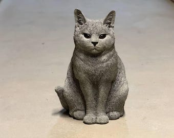 May include: A gray cat figurine with a sitting pose. The cat has a realistic appearance with fur details and black eyes.
