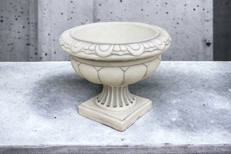 May include: A white ceramic planter with a decorative rim and a pedestal base. The planter is empty and ready for planting.